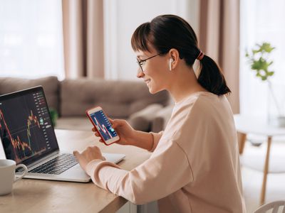 Female trader looking at charts on laptop and mobile device